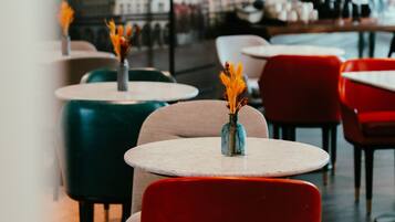 Un interior de restaurante con mesas y sillas redondas, algunas con jarrones de flores.