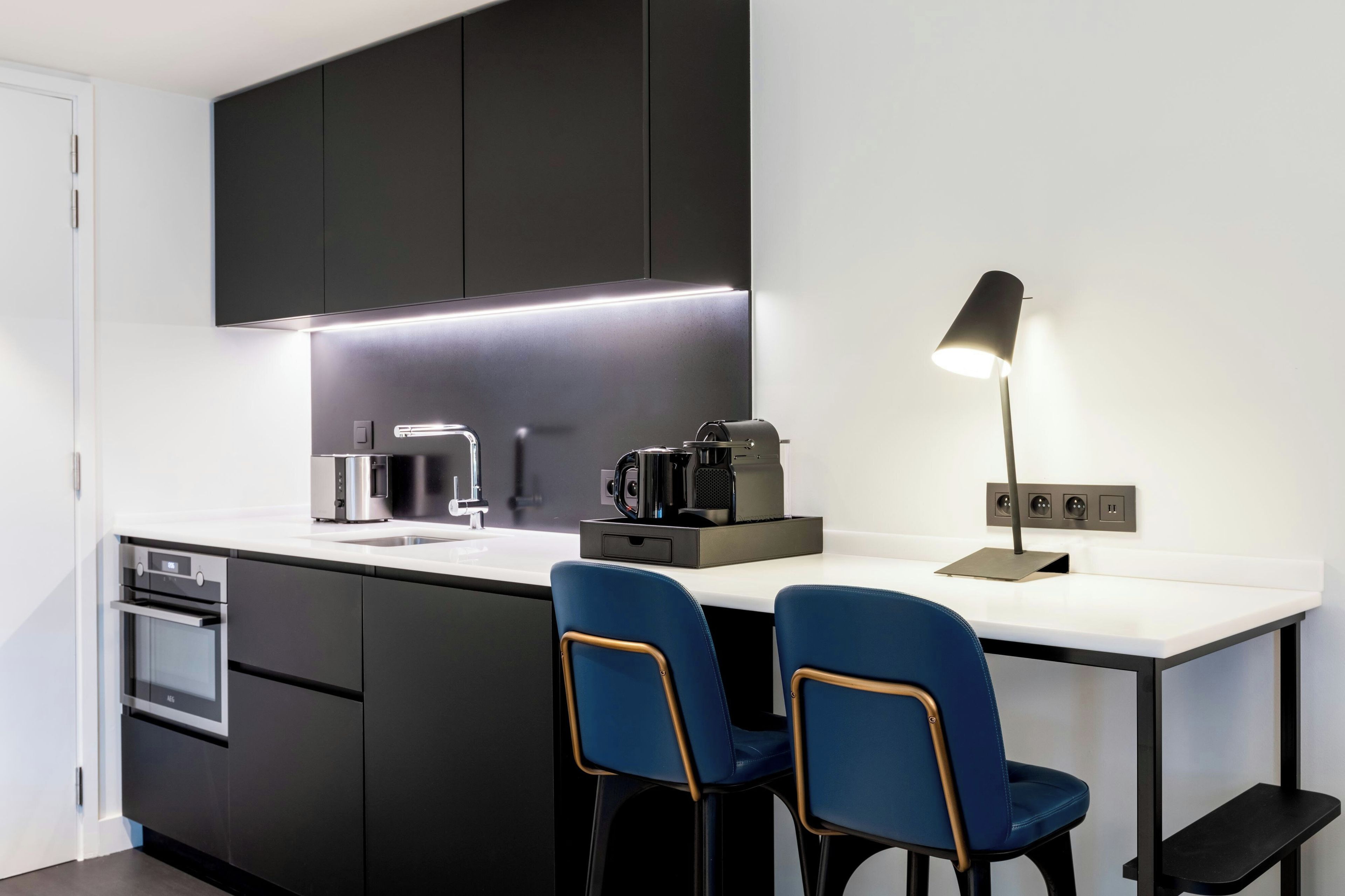 A modern kitchen with black cabinets, a white countertop, a coffee machine, and two blue chairs.