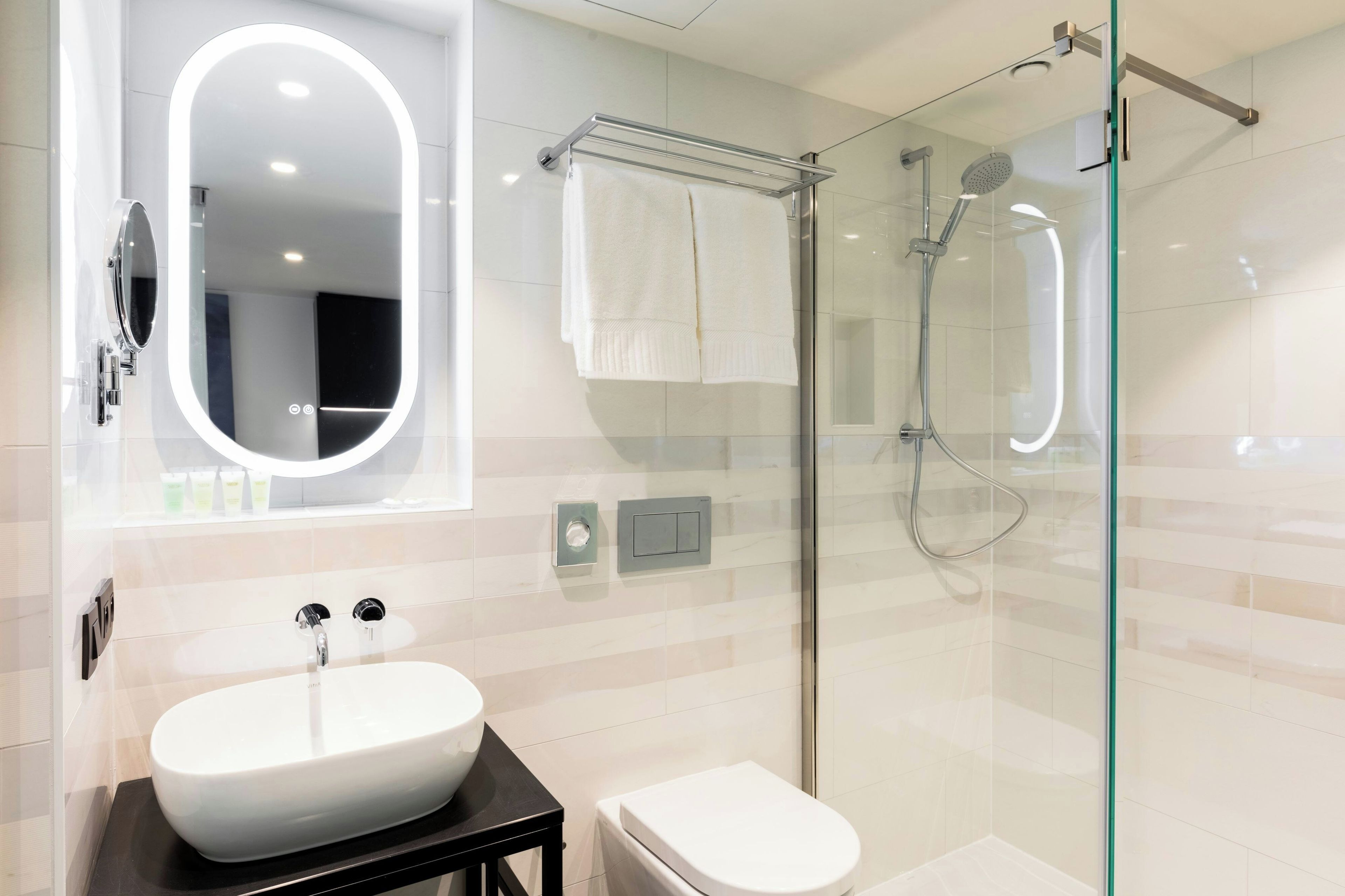 Un bagno moderno con un ampio specchio ovale, un lavandino bianco, un water e un box doccia in vetro.