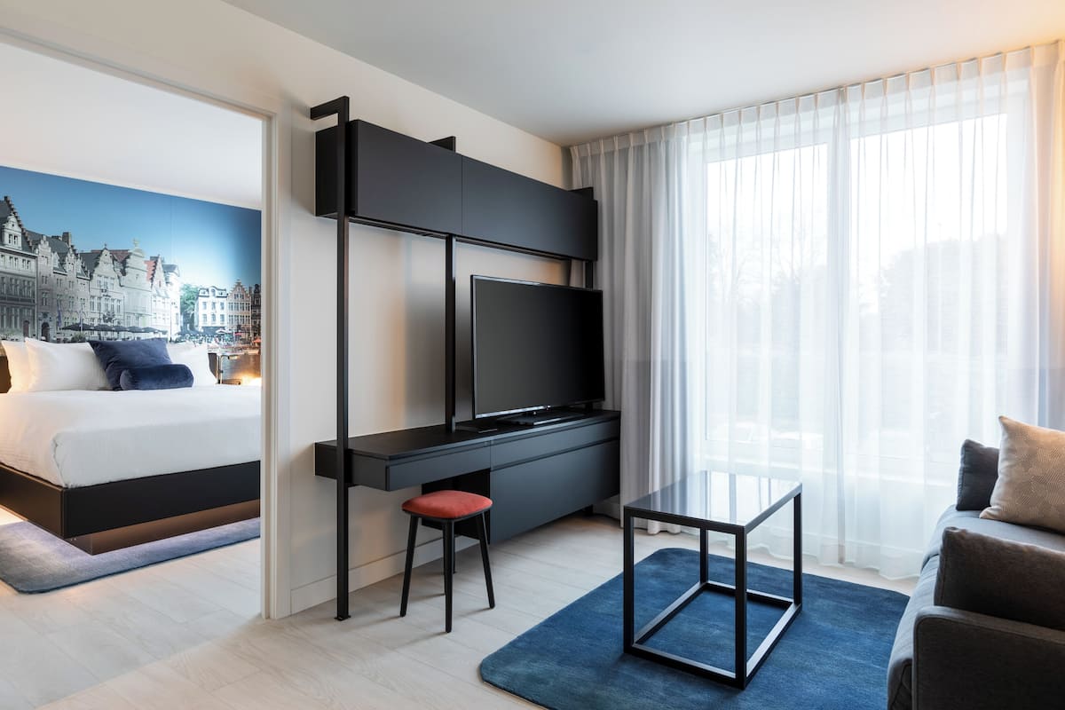 Ein modernes Hotelzimmer mit Bett, Schreibtisch mit Fernseher, kleinem Tisch und einer Sitzecke.