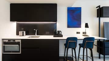 A modern kitchen with black cabinetry, a built-in oven, a coffee maker, and two blue bar stools.