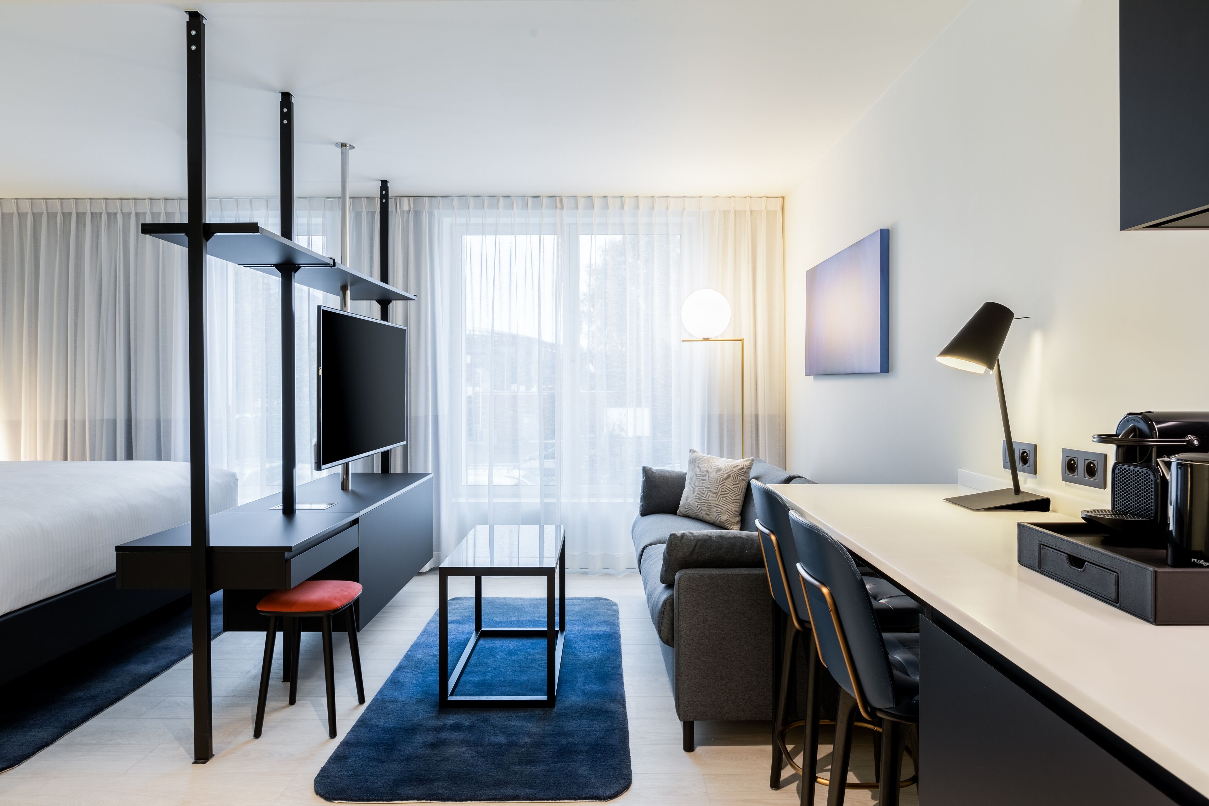 Quarto de hotel moderno com cama, escrivaninha e área de estar.
