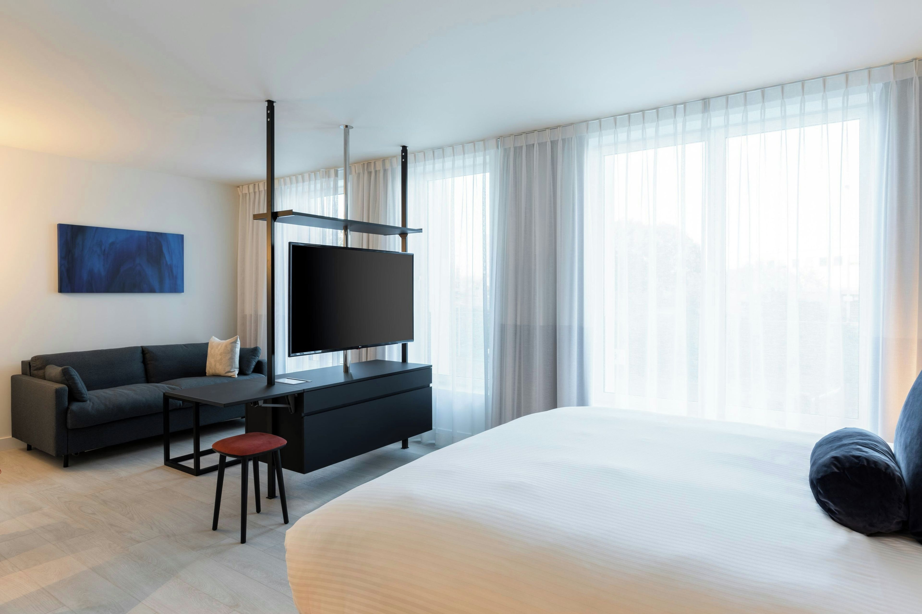 Une chambre d’hôtel moderne avec un grand lit, un téléviseur à écran plat, un canapé sombre et une petite table.