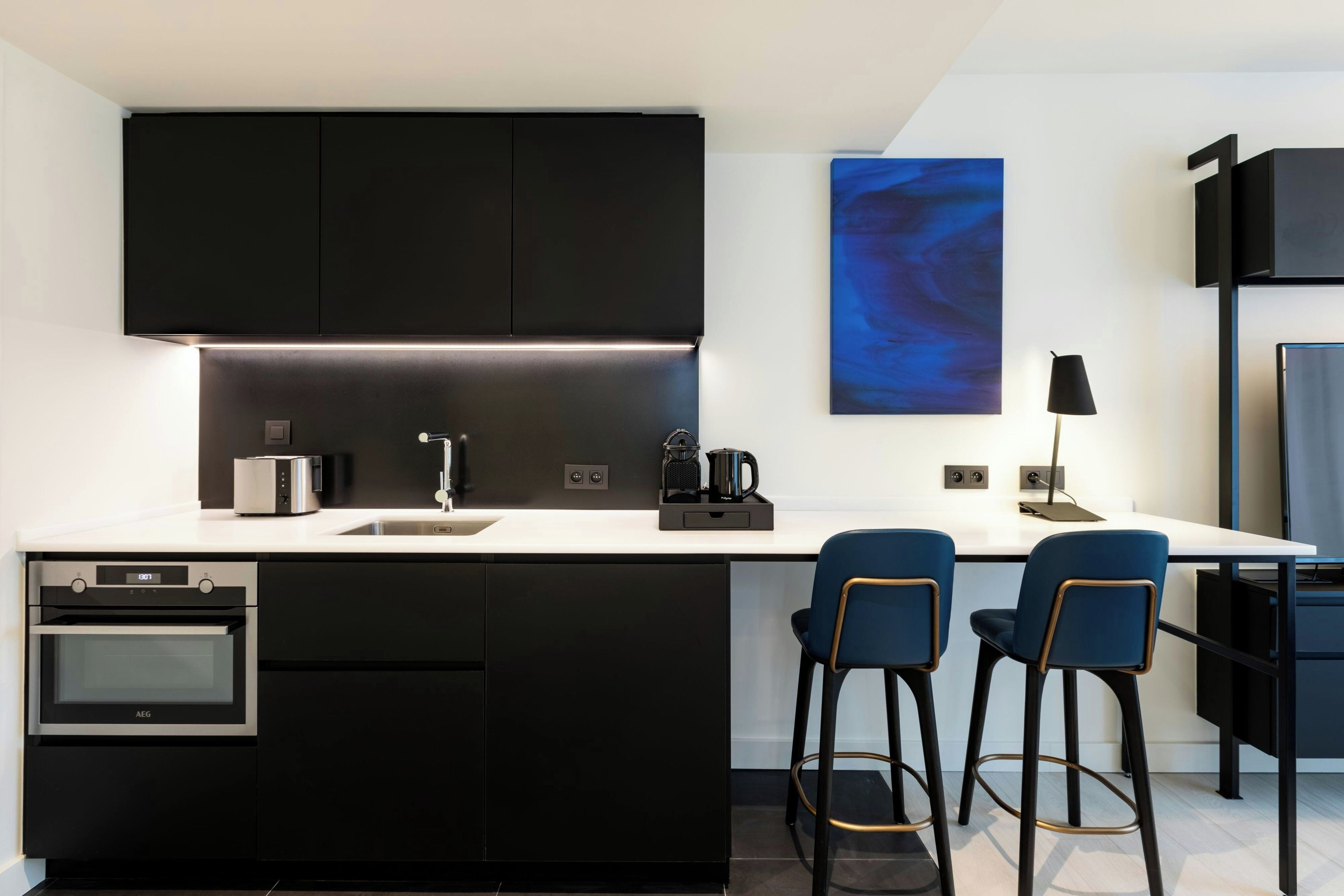 Eine moderne Küche mit schwarzen Schränken, einem eingebauten Backofen, einer Kaffeemaschine und zwei blauen Barhocker.