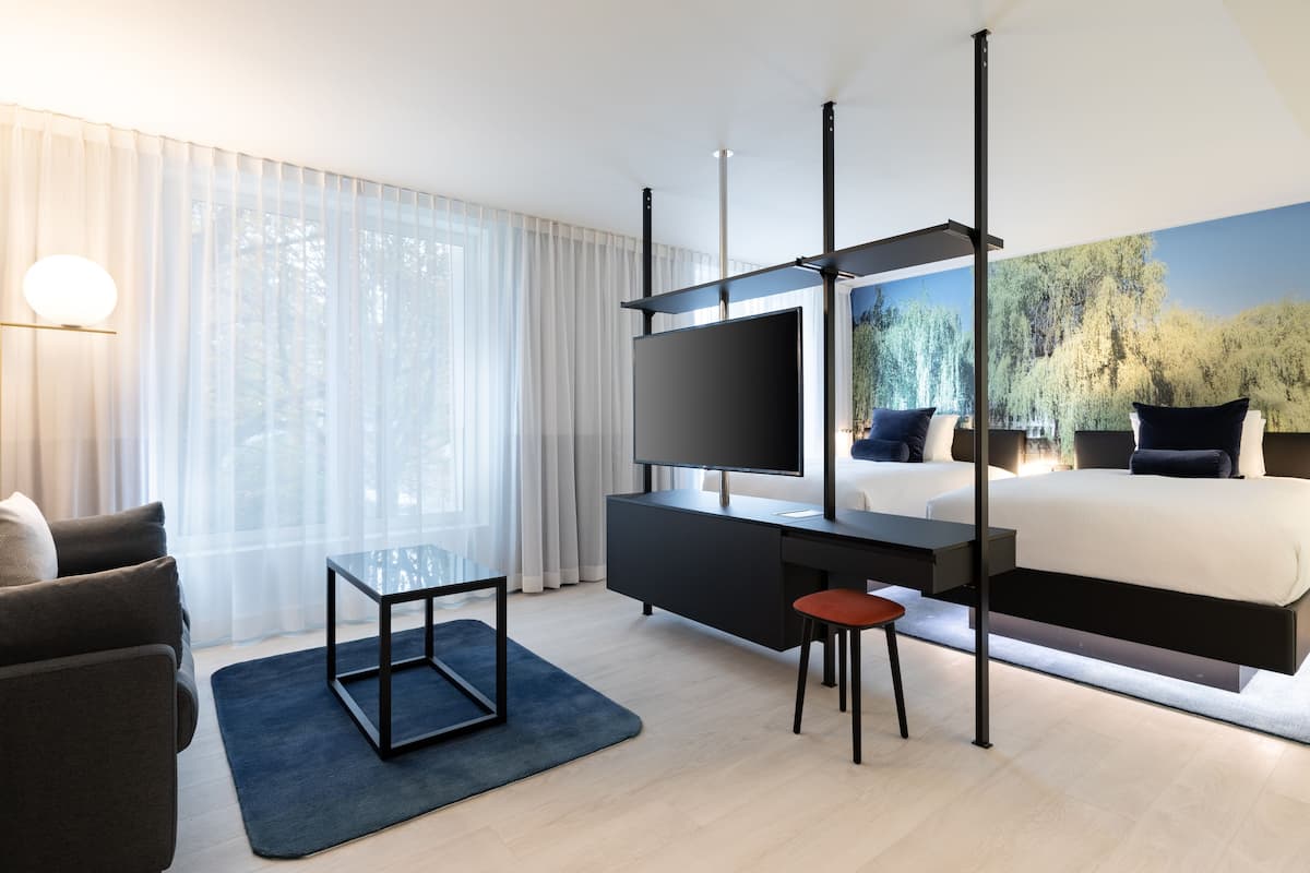 Ein modernes Hotelzimmer mit einem großen Bett, einem Flachbildfernseher, einem Schreibtisch und einem Sessel.