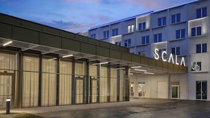 A modern hotel with a prominent 'SCALA' sign, large glass windows, and a covered entrance area.