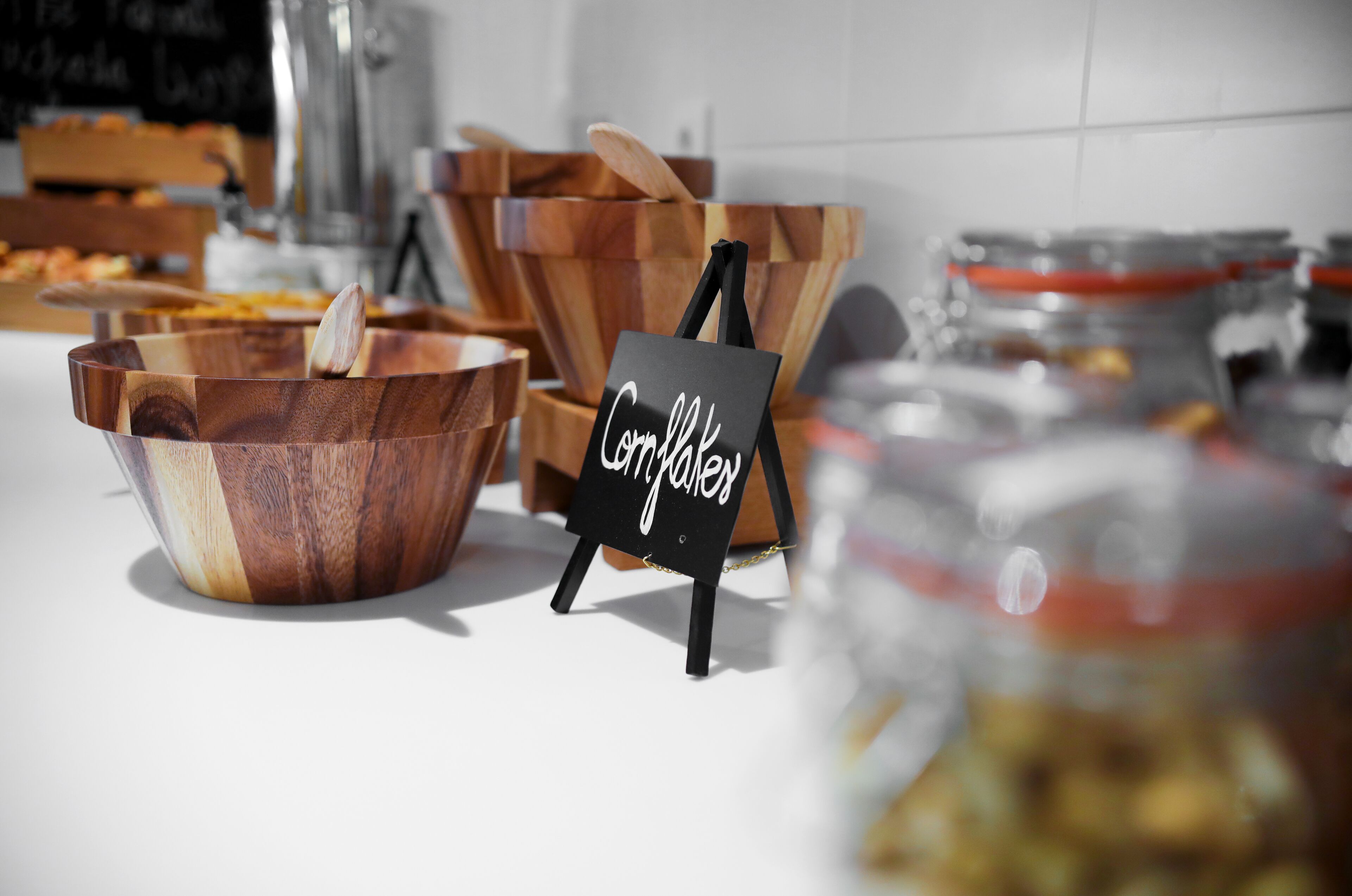 Eine Holtschale mit einem Schild, auf dem 'Cornflakes' steht, und im Hintergrund ein Honigglas.