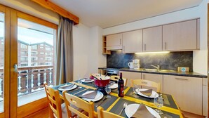 Ein Essbereich mit Tisch für vier Personen, eine Küche mit Holzschränken und ein Balkon mit Blick auf Gebäude.