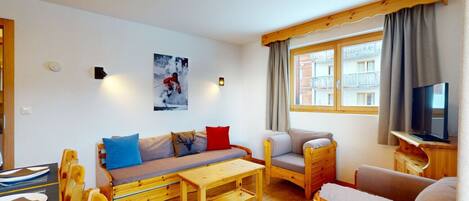 Une pièce confortable avec un canapé, une chaise en bois, une petite table et un téléviseur.