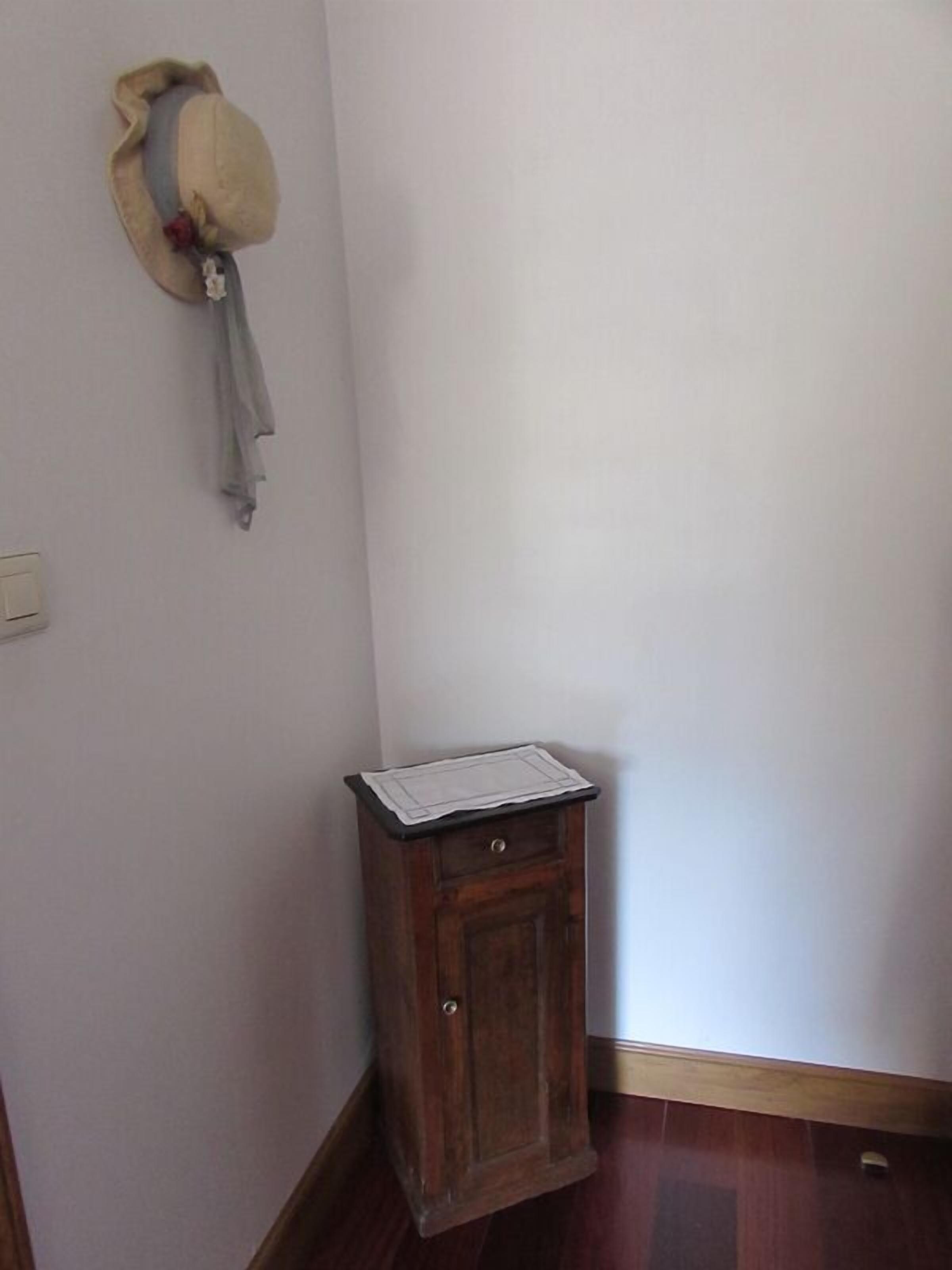 A corner room with a wooden cabinet, a hat on the wall, and a white door.