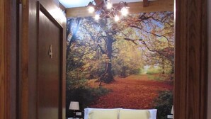 Un dormitorio con cama, mesita de noche, lámpara y un mural en la pared que representa un bosque.