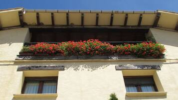 A building with a balcony with red flowers, two windows, and a yellow facade.
