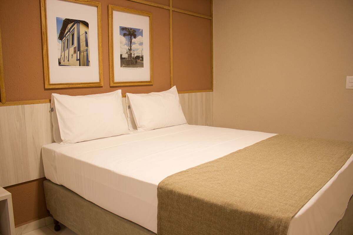 Een hotelkamer met een bed, een nachtkastje en twee ingelijste foto's aan de muur.