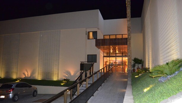 Un edificio moderno con una escalera que lleva a una entrada con puerta, un coche estacionado al frente y un camino bien iluminado.