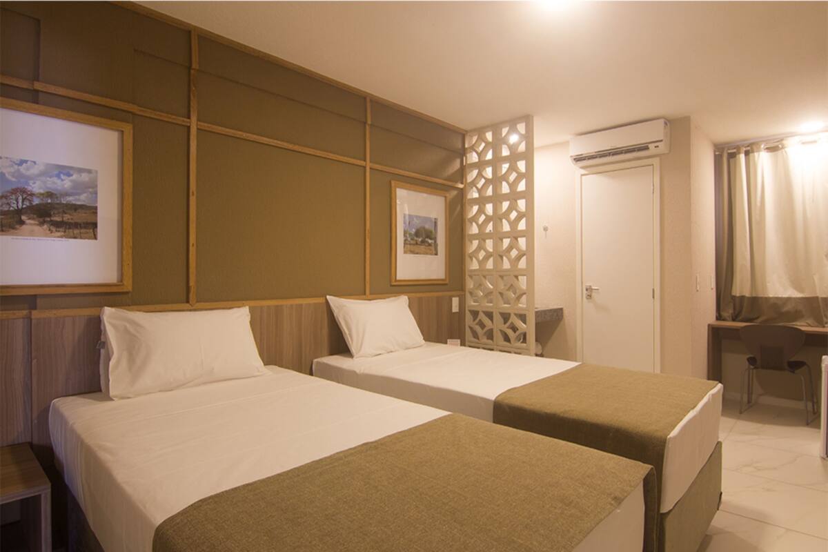 Een hotelkamer met twee bedden, een bureau, een airconditioning en een decoratieve scheidingswand.