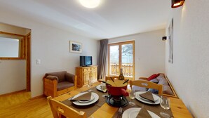 Un comedor acogedor con una mesa de madera preparada para dos personas, un sofá y un televisor sobre un mueble de madera.