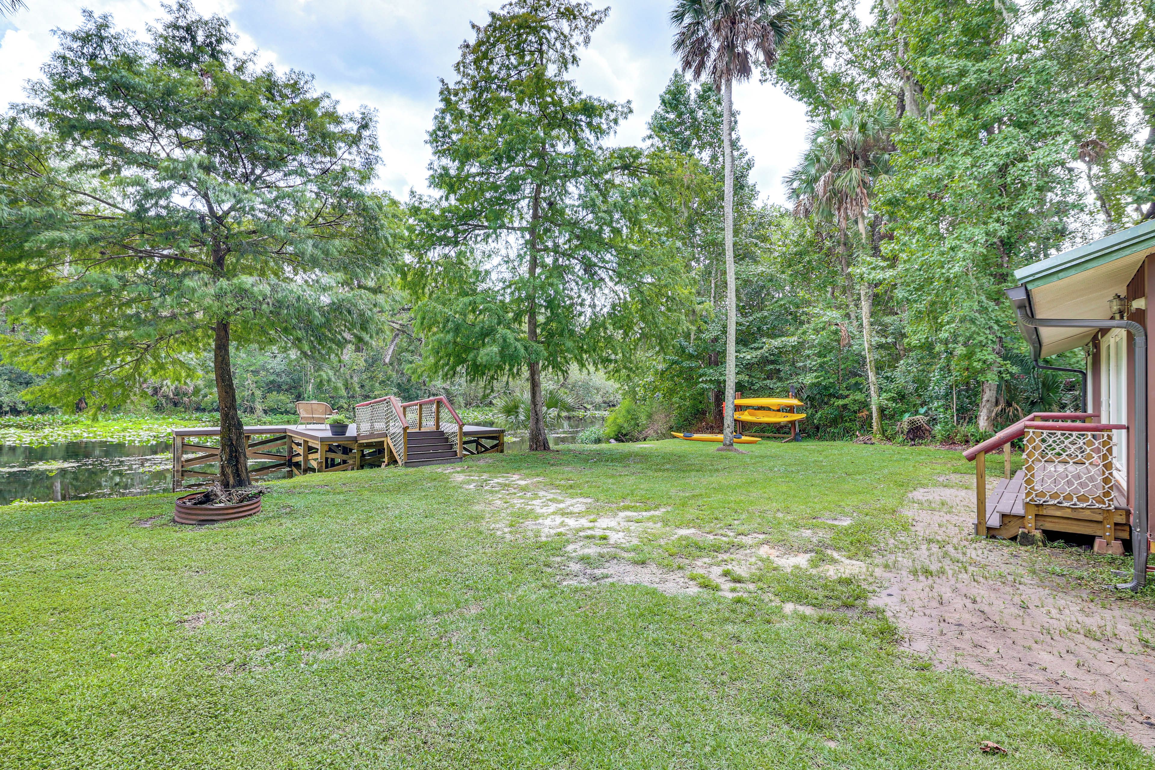 A garden with a wooden deck, a small table, and chairs. There is a yellow kayak and a paddleboard near the water.