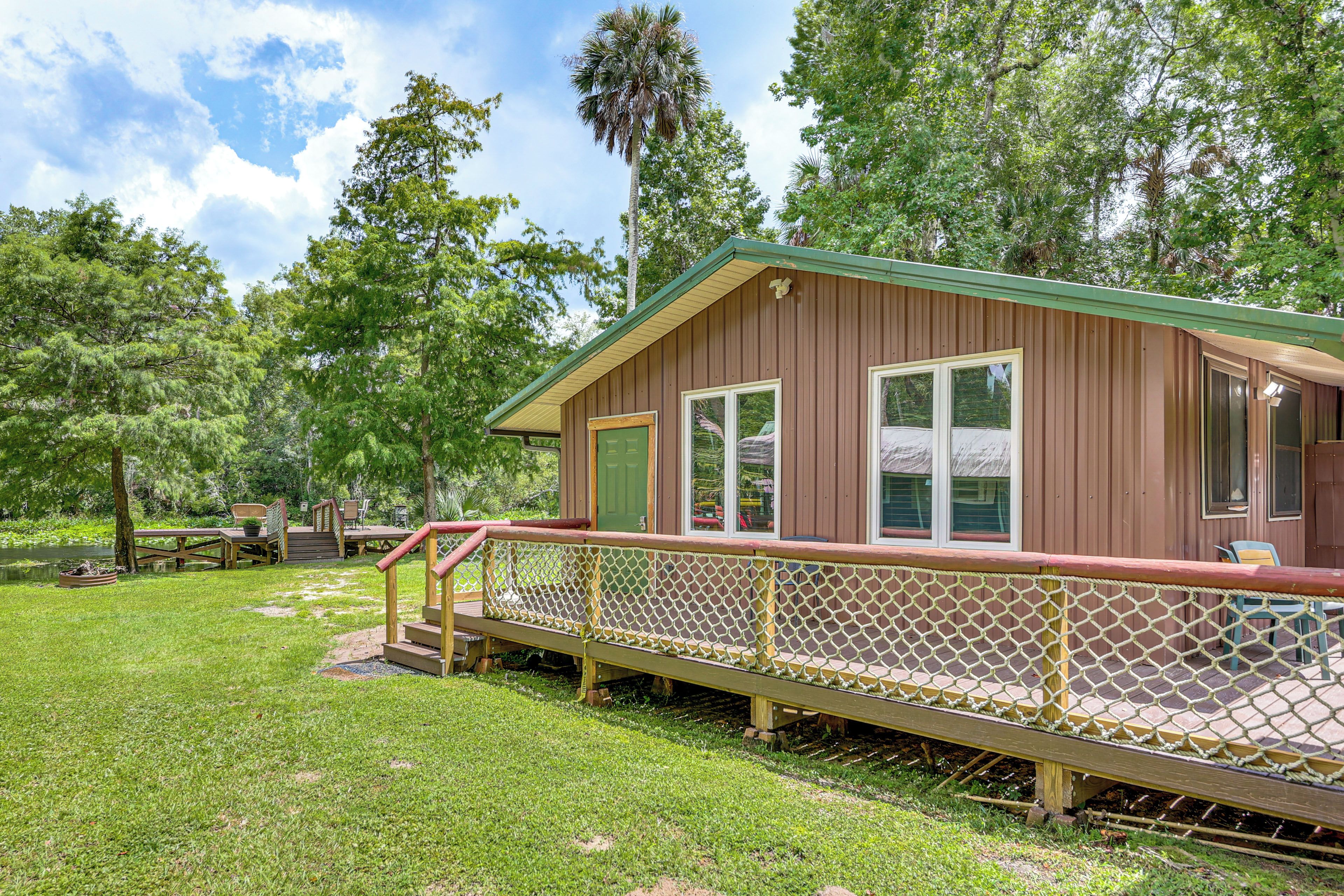 A wooden cabin with a deck, surrounded by trees and a grassy area.