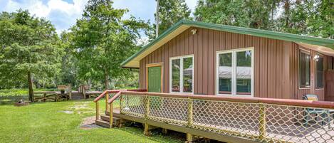 A wooden cabin with a deck, surrounded by trees and a grassy area.