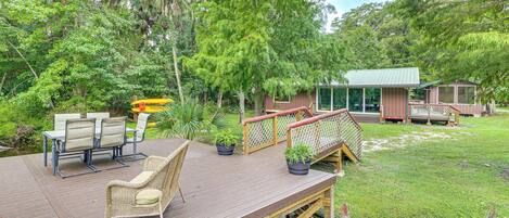 A wooden deck with outdoor furniture, a small bridge, and a building with a green roof.