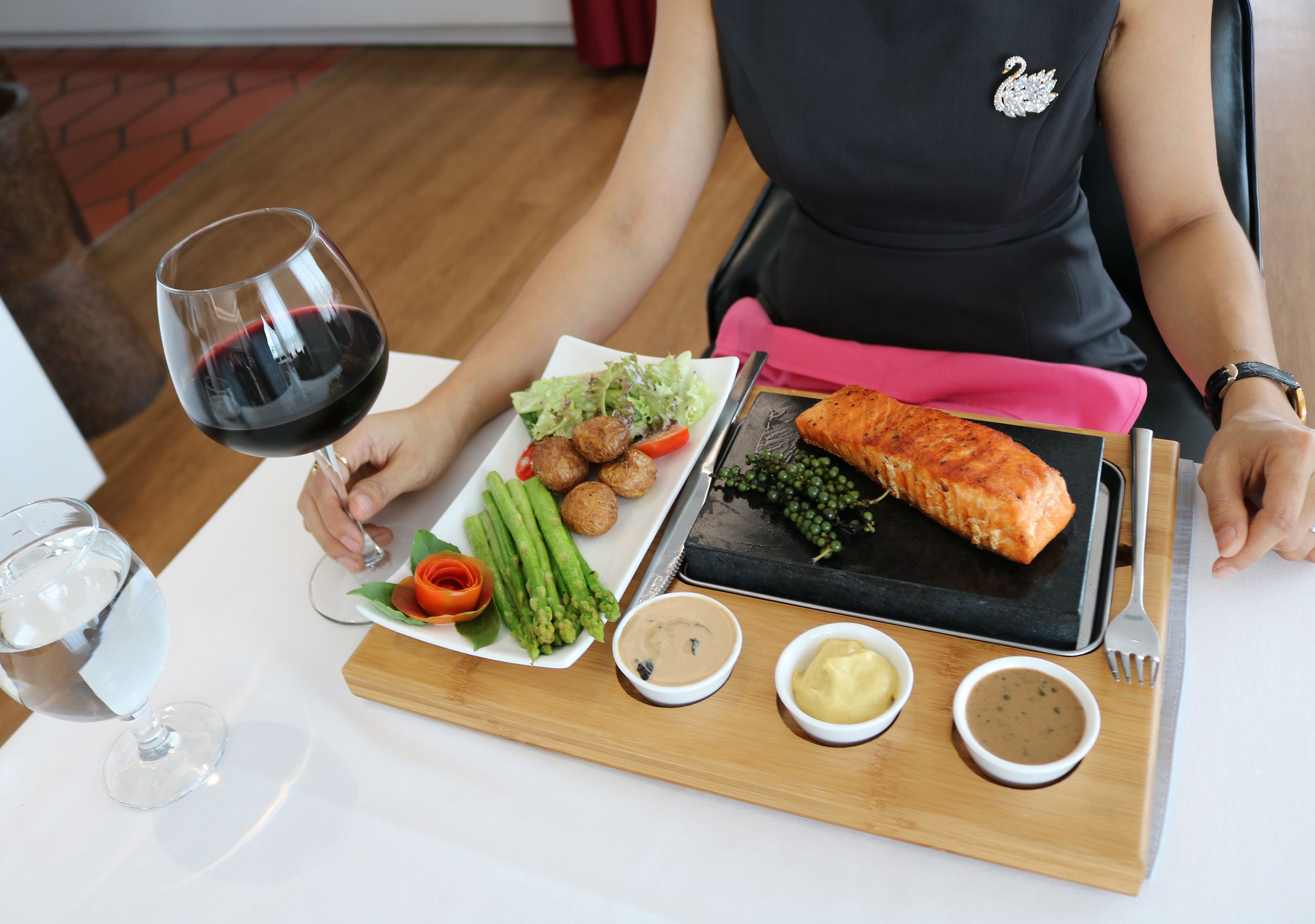 Une table à manger avec une assiette de nourriture, un verre de vin rouge et une planche à découper en bois sur laquelle sont disposés divers condiments.