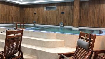 A spa area with a hot tub, wooden walls, and steps leading to the tub. There are wooden chairs and a small table near the tub.
