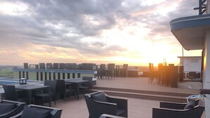 Een dakterras met zitplaatsen buiten en uitzicht op de ondergaande zon.