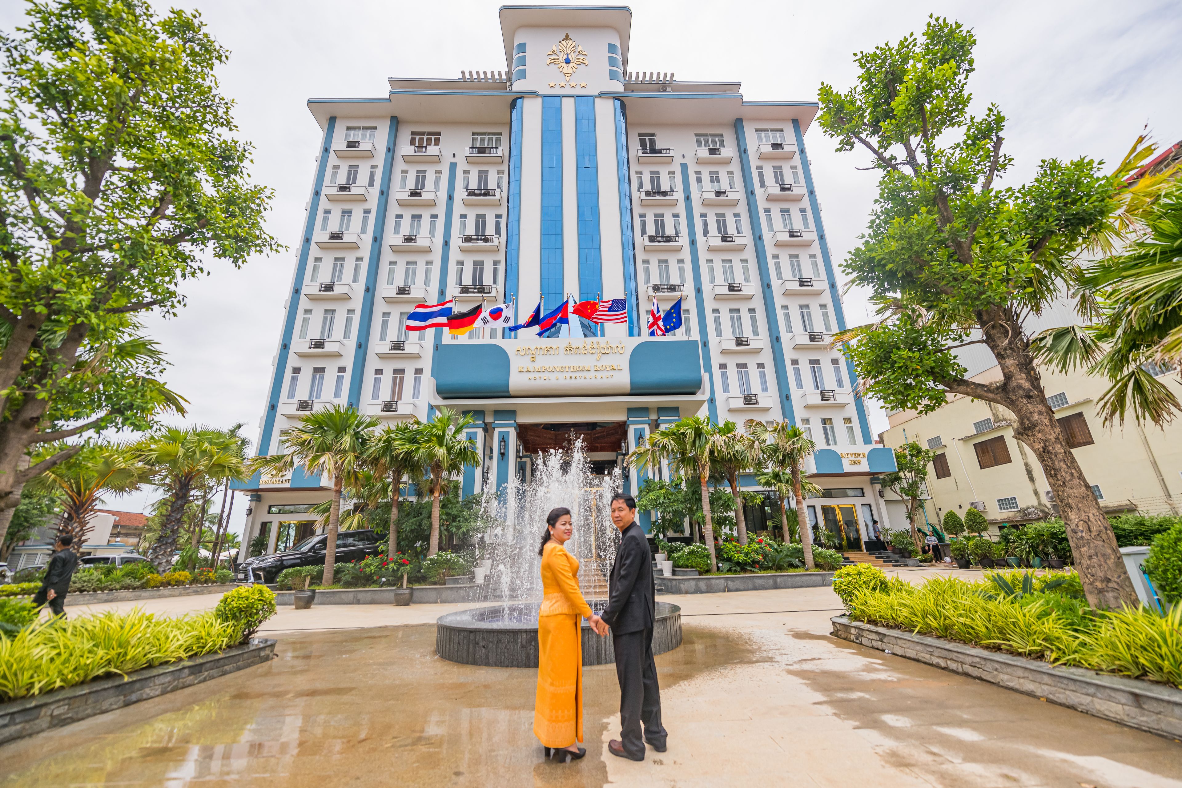 A hotel with a fountain, palm trees, and flags.