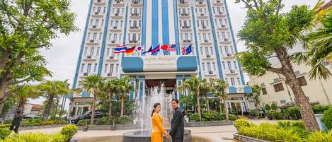 A hotel with a fountain, palm trees, and flags.