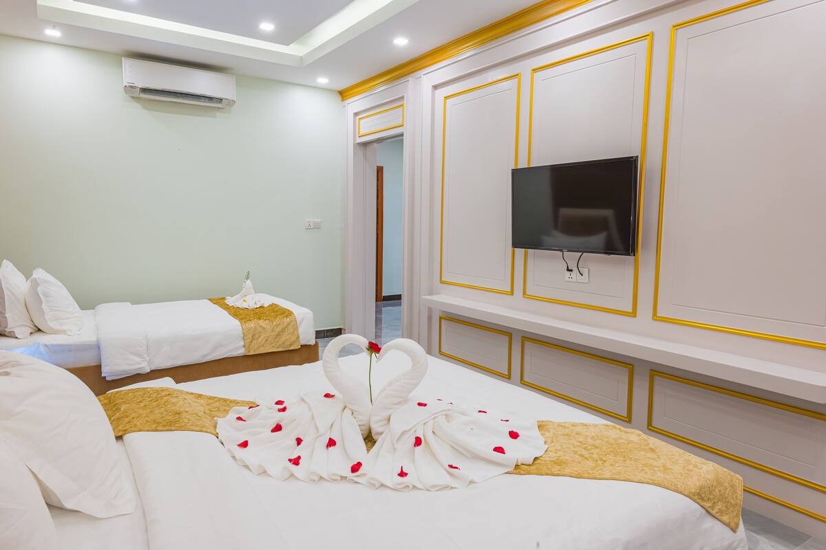 Ein Hotelzimmer mit zwei Betten, einem an der Wand befestigten Fernseher und einer aus Handtüchern geformten Schwane auf dem Bett.