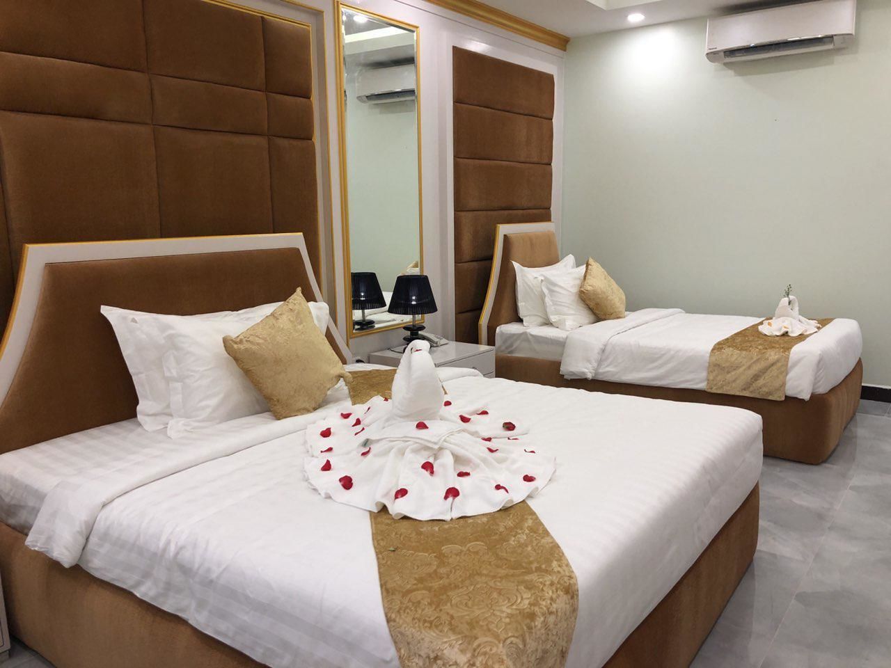 A hotel room with two beds, each with a headboard, white bedding, and a decorative white cloth with red rose petals.