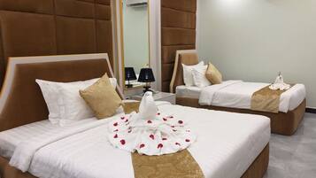 A hotel room with two beds, each with a headboard, white bedding, and a decorative white cloth with red rose petals.