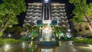 Een meerlaags hotel met een centrale fontein, omgeven door weelderig groen en verlicht met kunstlicht.