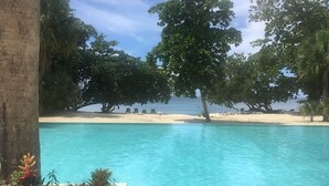 Una piscina cristallina con una spiaggia sabbiosa e sedie a sdraio sullo sfondo.