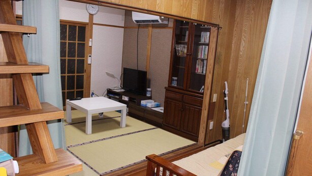 Een traditionele Japanse kamer met tatami vloerbedekking, een lage houten tafel, een televisie, een boekenplank en een schuifdeur.