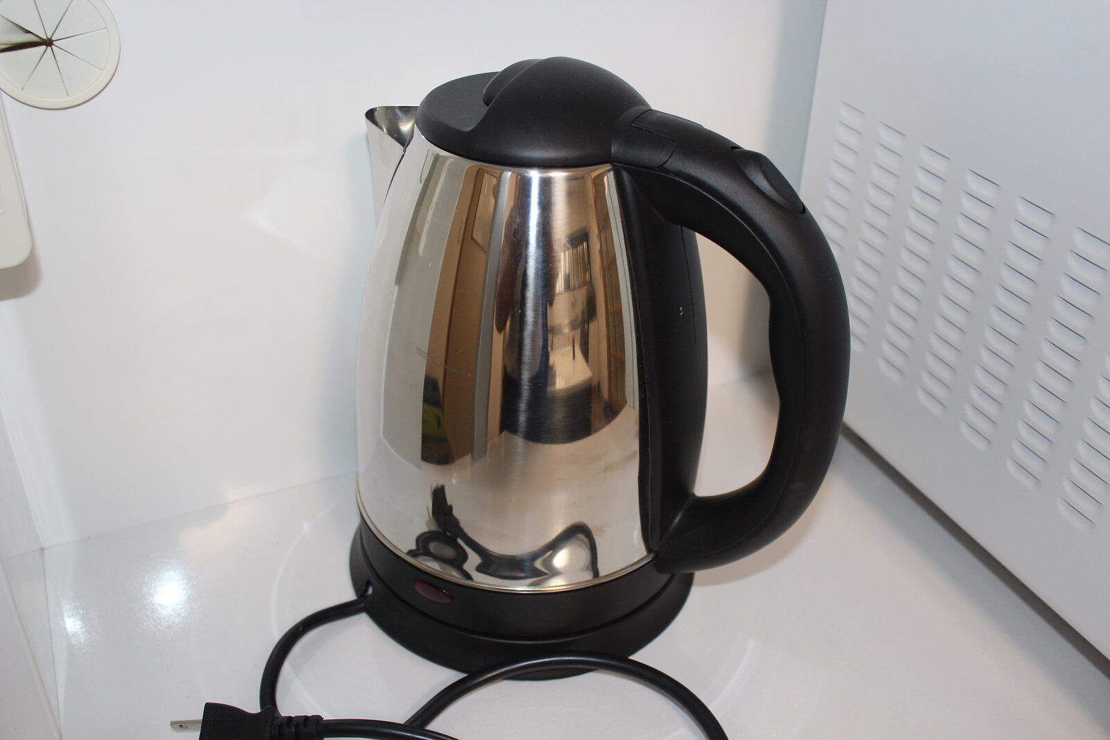 A stainless steel electric kettle with a black handle and cord on a white countertop.