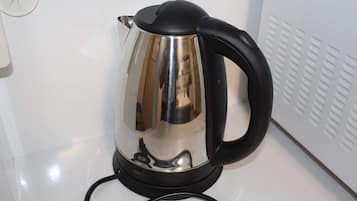 A stainless steel electric kettle with a black handle and cord on a white countertop.