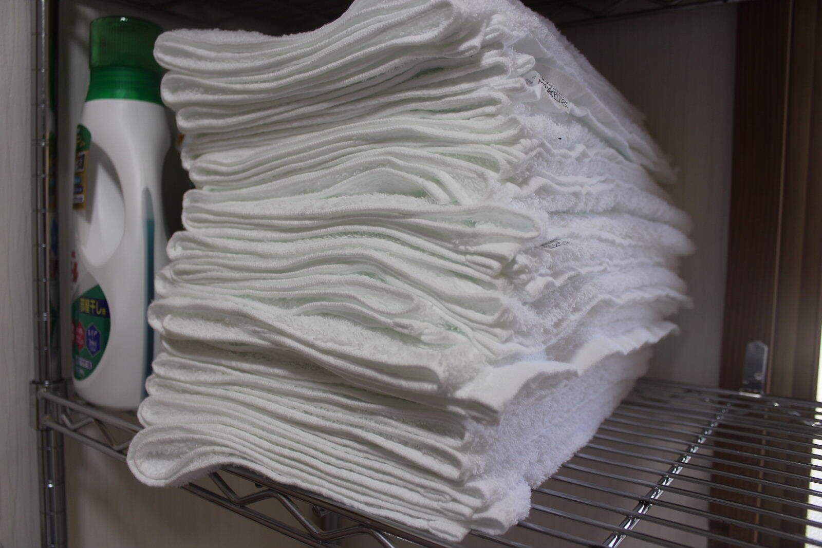 Une étagère avec des serviettes blanches soigneusement pliées et une bouteille de savon liquide.