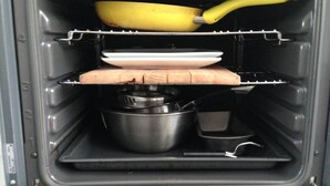 En öppen ugn med en banan i, en tallrik, en skärbräda i trä och en kastrull.