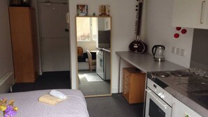 Ett litet hotellrum med en säng, ett minikök, en gitarr och en spegel.