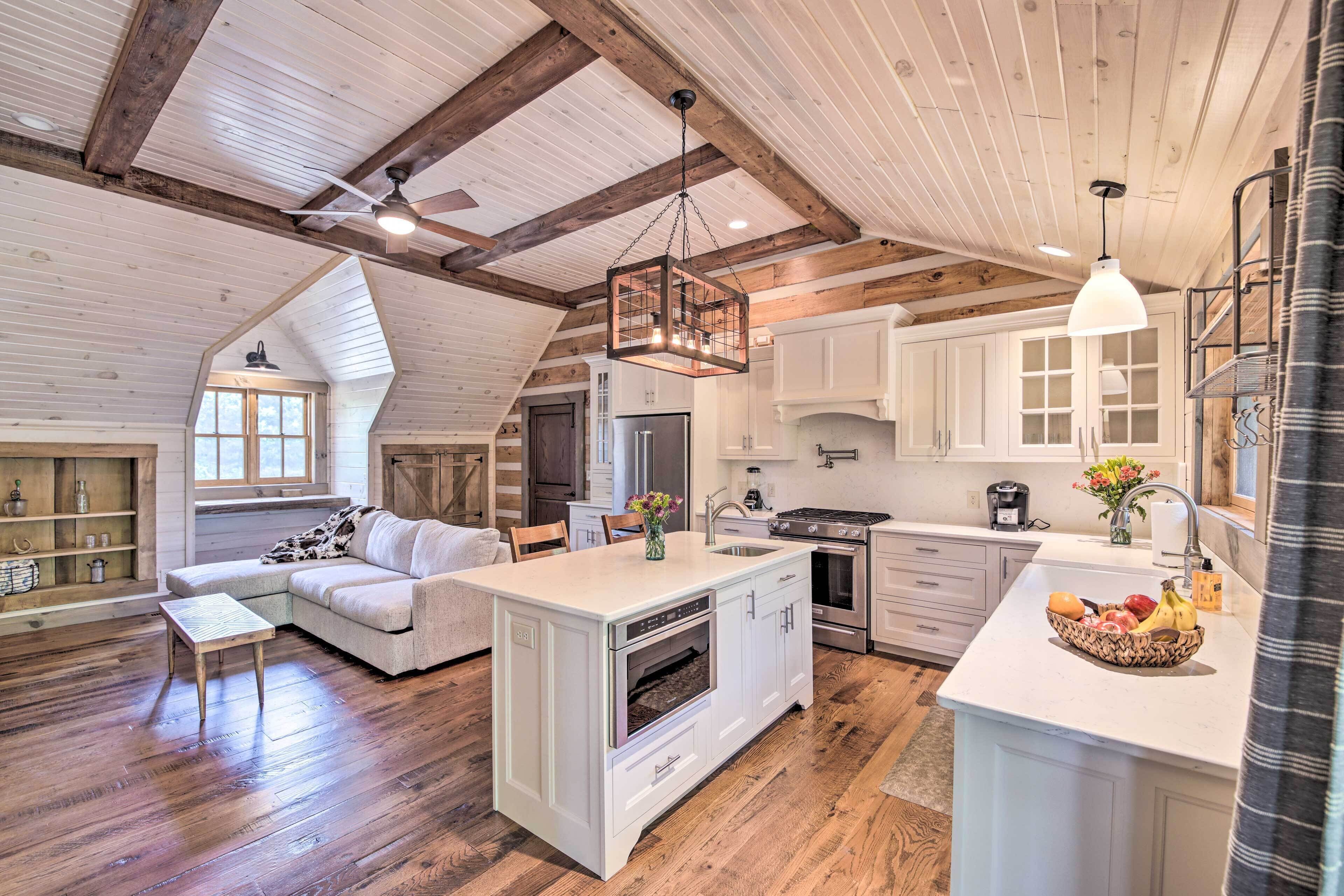 Un'ampia cucina in stile loft con mobili bianchi, una grande isola con forno integrato e un'area pranzo con tavolo in legno e divano.