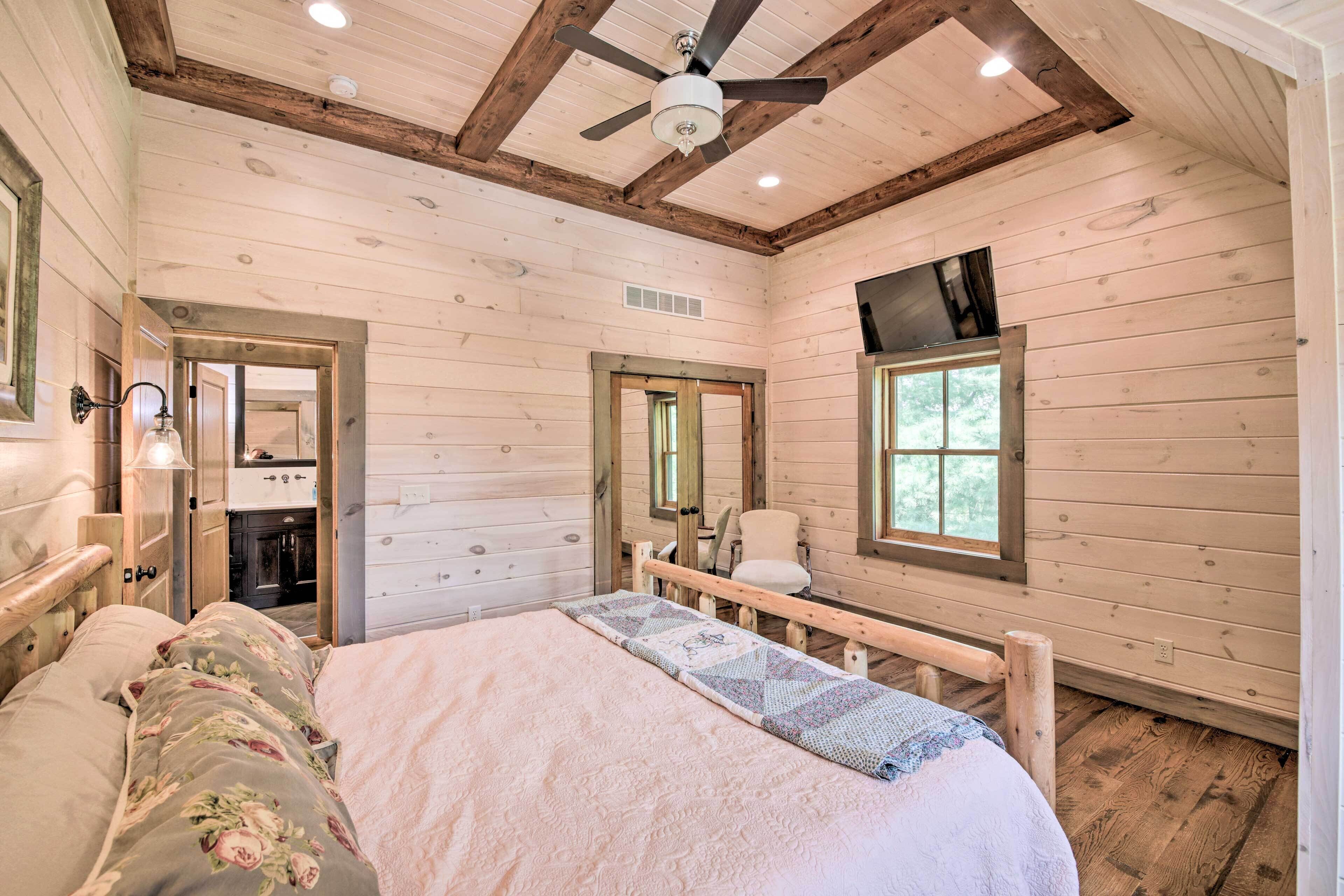 A wooden cabin bedroom with a bed, a ceiling fan, a window, and a door leading to a bathroom.