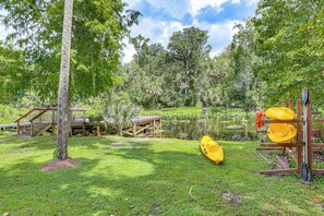 A grassy area with a wooden deck, a yellow kayak, and a paddleboard on a wooden stand.