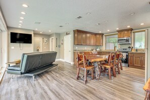 Una cocina amplia con armarios de madera, un comedor con mesa y sillas de madera, un horno integrado y un televisor de pantalla plana montado en la pared.