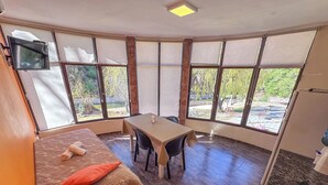 Une pièce comprenant un lit, une table et des chaises, de grandes fenêtres avec des rideaux et un luminaire au plafond.