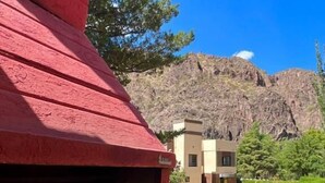 Un espace extérieur doté d’un toit rouge, comprenant un barbecue, une piscine et, en arrière-plan, une montagne.