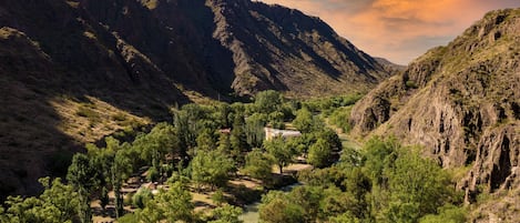 A mountainous landscape with a river, a small building surrounded by trees, and steep cliffs.