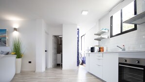 Una cocina moderna con armarios blancos, horno integrado y encimera con tetera y otros electrodomésticos.