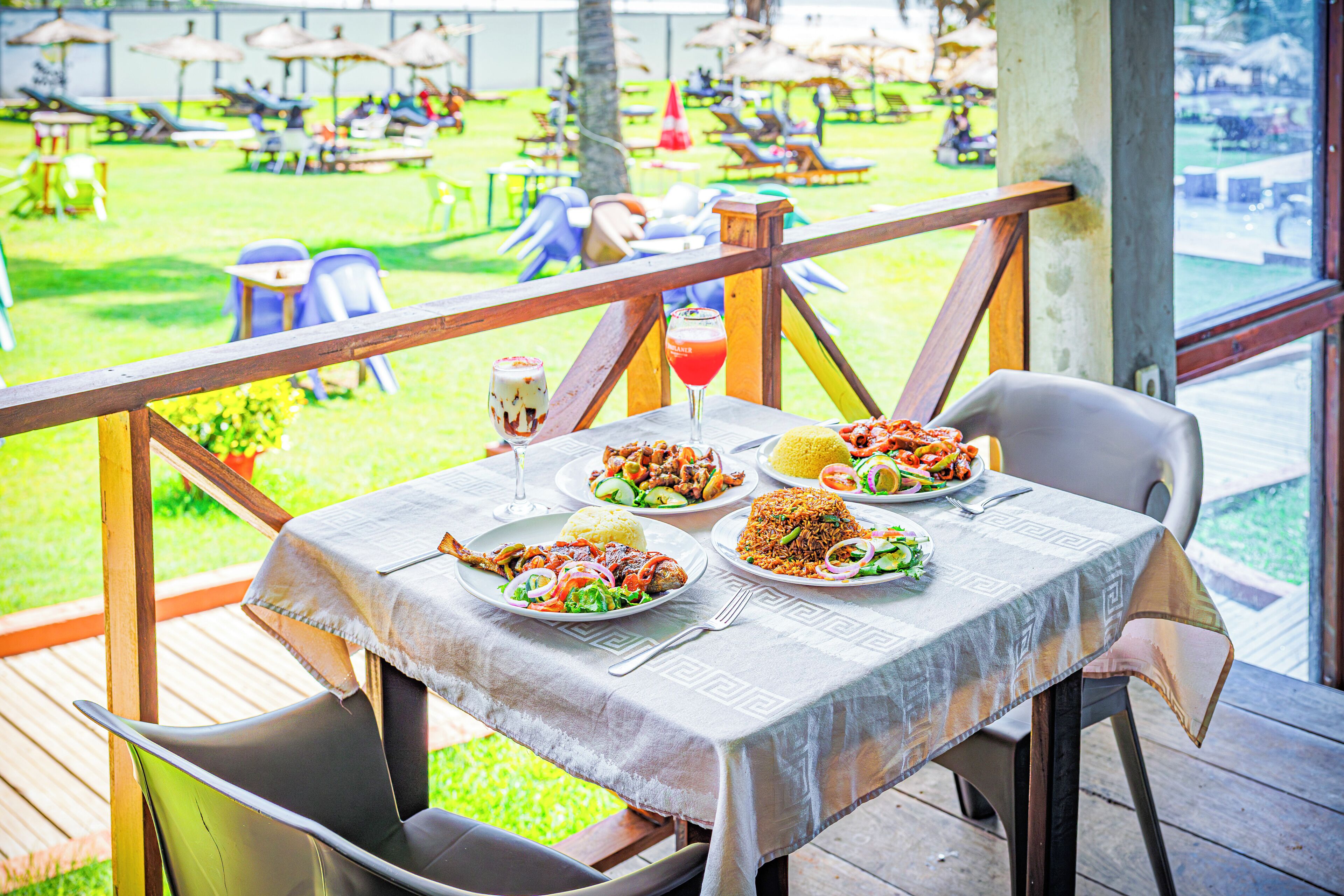 A dining area with a table set for four, overlooking a grassy outdoor space with umbrellas and lounge chairs.