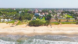 An aerial view of a coastal area with a beach, palm trees, and buildings. - Kasumai Beach Resort (Serrekunda)